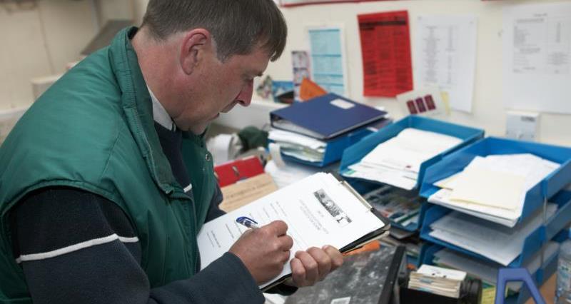An image of a man in an office filling out paperwork on a clipboard