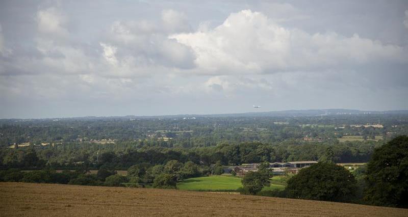 A view across farmland with trees, hedgerows and residential areas in the distance 