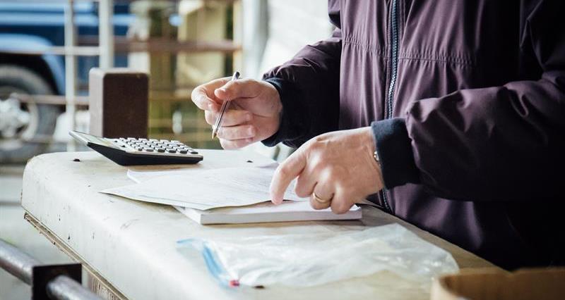 A image of a man in overalls outdoors on a farm looking at paperwork