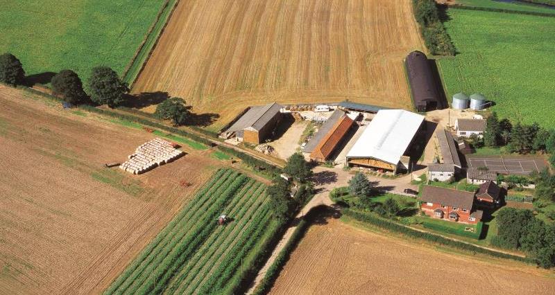 An aerial view of farmland, farm buildings, harvested fields and a river running through the fields.