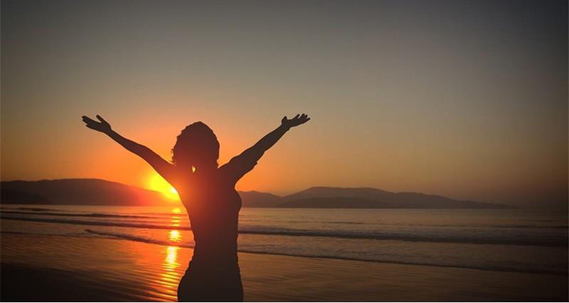 Young lady on a beach at sunset with arms raised