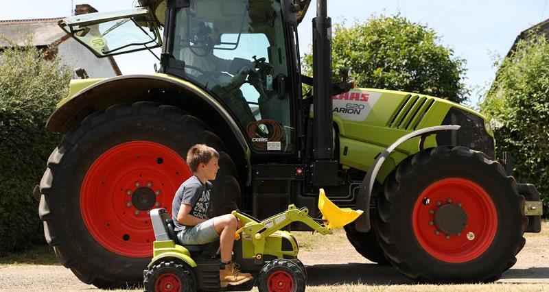 A child driving a toy tractor with a tractor in the background