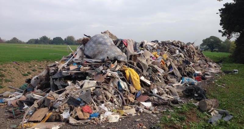 A huge pile of rubbish, including household items such as mattresses, piled high on an area of farm land