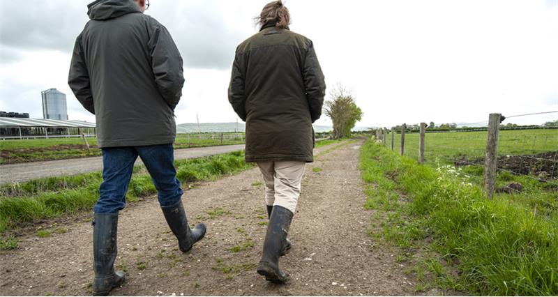An image of two farmers talking as they walk along a farm path