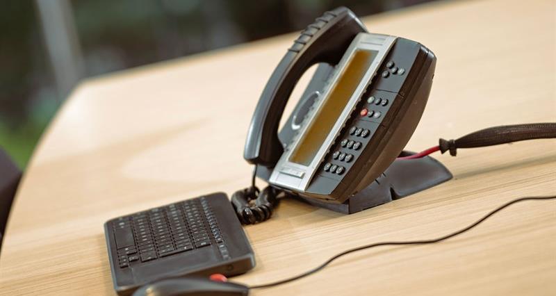 An analogue telephone on a desk alongisde a keyboard and mouse