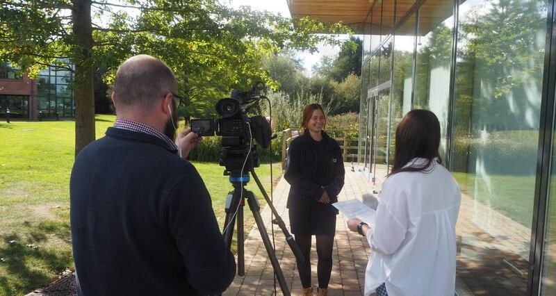 A photo of a poultry industry programme participant getting involved with media training. She is standing in front of a cameraman and interviewer.