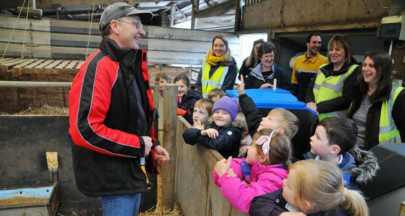 A group of primary school children grouped around a farmer in a housing shed