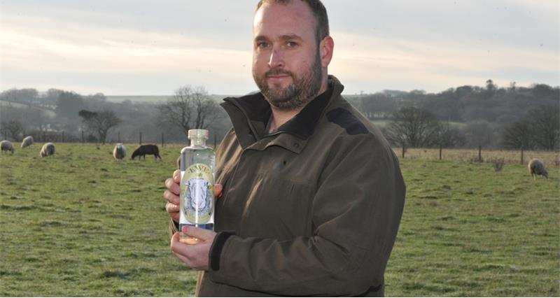 A photo of Bryn Perry posing with a bottle of his vodka. 