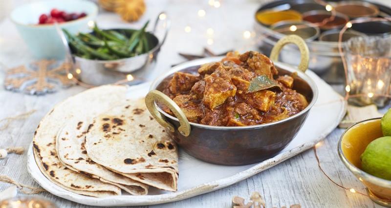 An image of turkey curry with naan bread on a ceramic dish. 