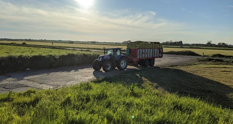A tractor towing a forage wagon along a road with the sun setting in the background