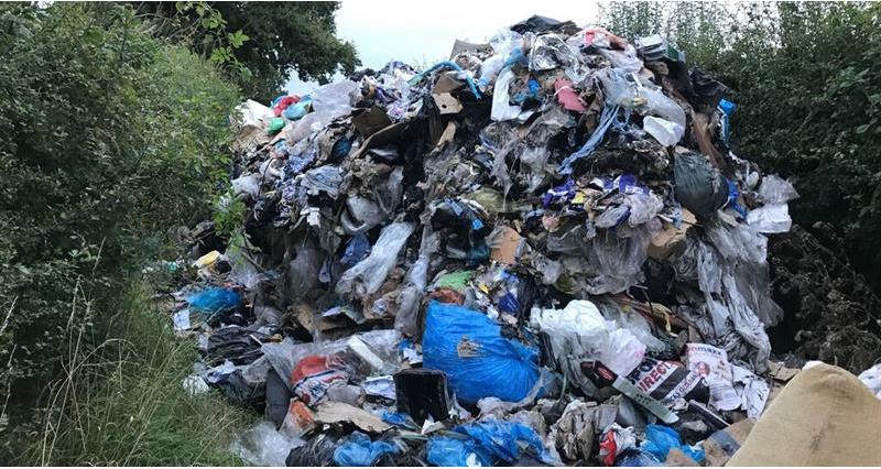 A picture of a huge pile of illegally dumped waste on farmland