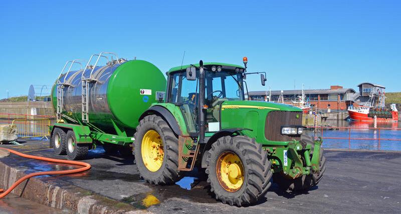 A green John Dere tractor with a green fuel bowser attached to it.