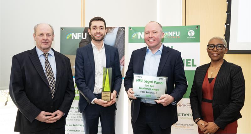 A group of four people standing in front of legal panel banners, the middle two are holding awards