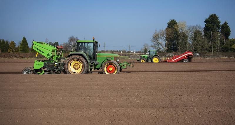 Two green tractors driving across a ploughed field.
