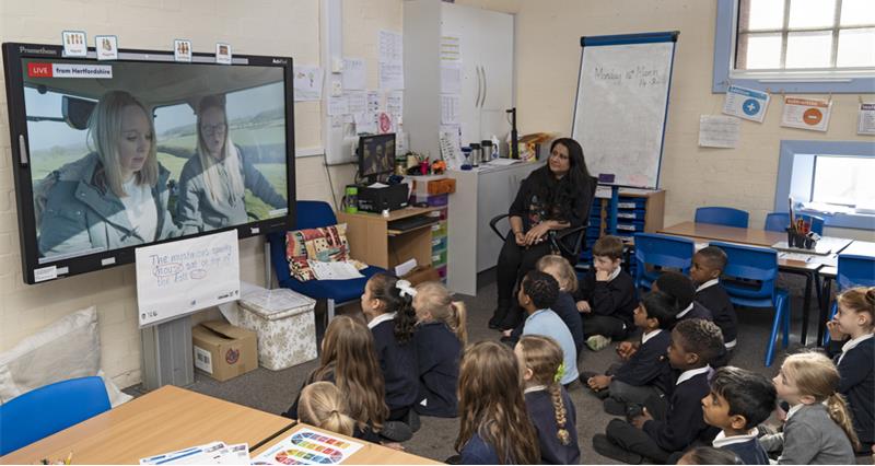 An image of a class of primary school children with their teacher , watching Science Farm Live on a screen in their classroom. 
