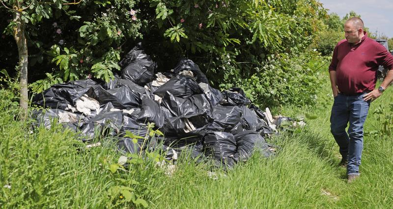 A male farmer observing a large pile of rubbish dumped in his feild