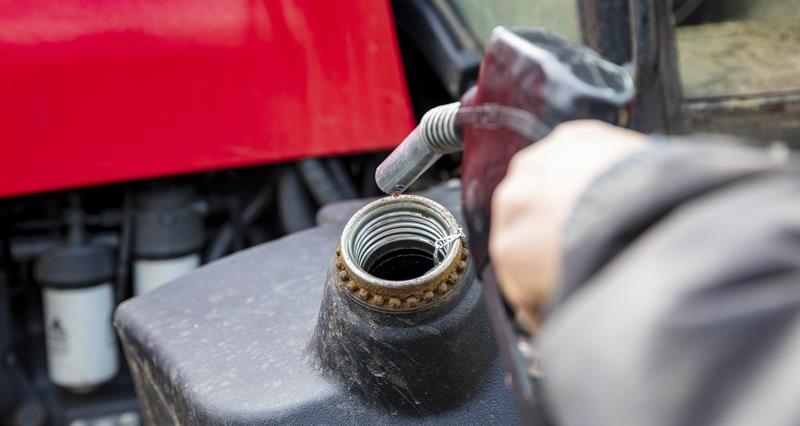 A person holding a fuel nozzle over a recepticle