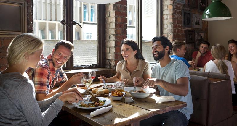 A group of men and women sat around a restaurant table laughing and eating