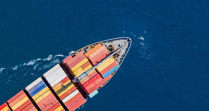 An overhead picture of a ship sailing through the sea carrying multi-coloured shipment containers