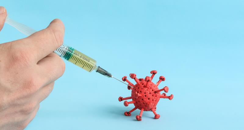 An image of a vaccine being injected into a red virus particle 