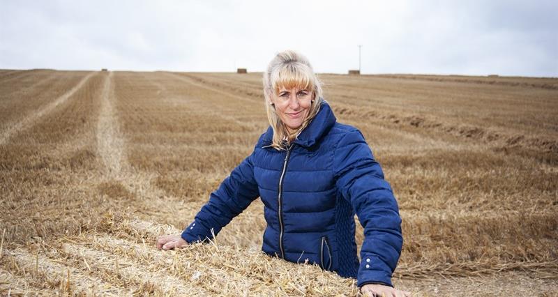 A picture of Minette Batters stood in a harvested field leaning on a bale of straw
