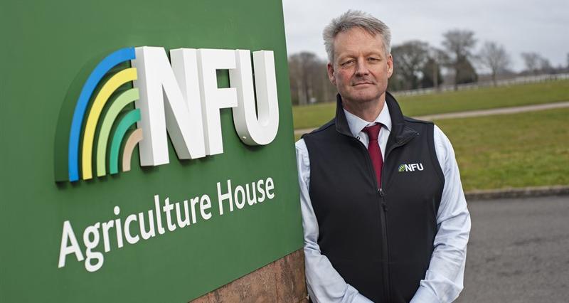 A picture of David Exwood leaning on the NFU's sign outside of its headquarters