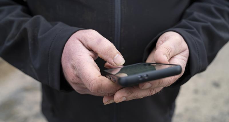 A close up photo of a farmer viewing smartphone on farm