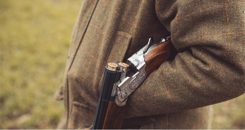 A shotgun open broken over hunter forearm wearing traditional English clothing