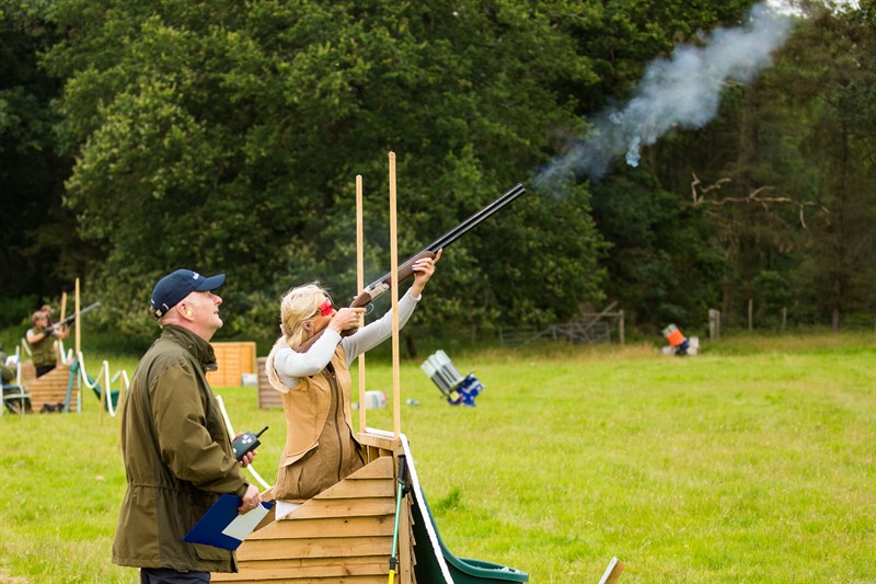 A person firing a gun at clay pigeons watched by another person at a game fair