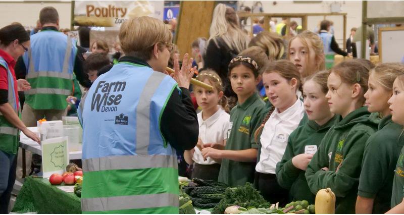 Children standing at a table in front of a display of vegetables
