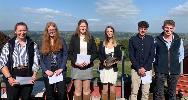 A group of young people standing outside, holding award certificates. One also has a trophy.