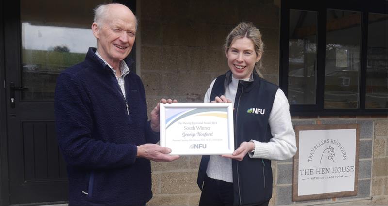 Two people holding an award certifcate, standing in front of a building