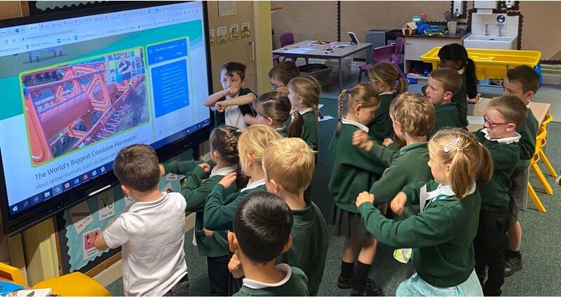 A picture of a group of school children stood up and spinning their arms as part of a harvest live lesson on a tv screen