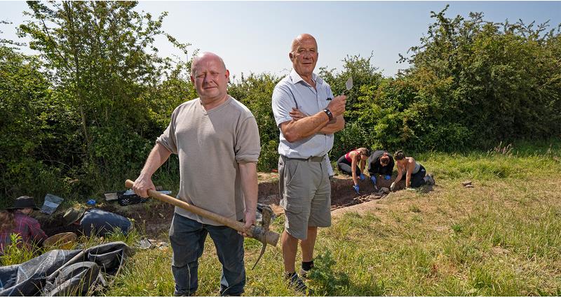 An image of Gerry and Richard Fair holding hammers stood in front of their digging site