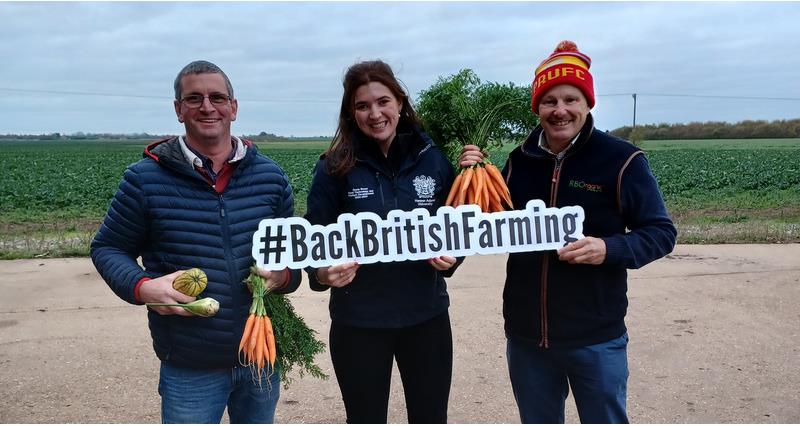 NFU Organics Forum member Adam Westaway (left), former NFU placement student Grace Brown (centre) and Andrew Burgess (right). They are holding organic vegetables and an NFU 'Back British Farming' sign.