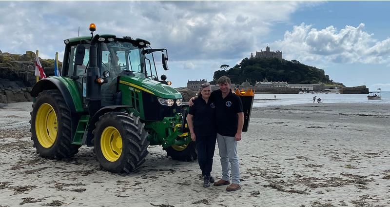 A photo of Lynda and Andy Eadon on a beach in Cornwall. To the left of them is the len's light tractor. 