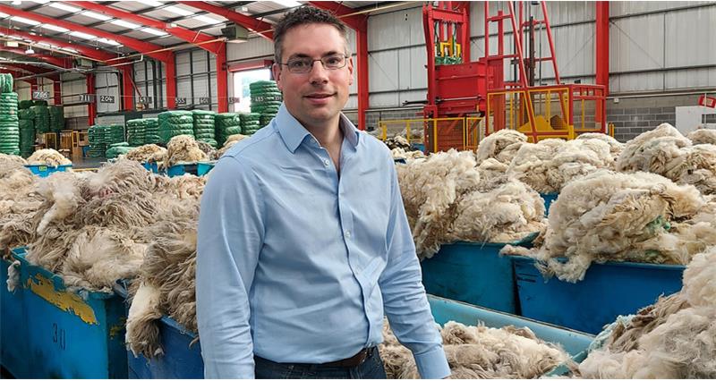 A photo of Andrew Hogley, Chief Executive of British Wool. He is pictured in a blue shirt, in a factory surrounded by sheep wool.