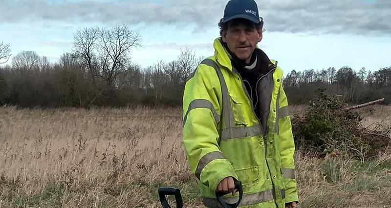 An image of Huw Rowlands on farm. He is wearing a large hi-vis jacket and is holding a spade.