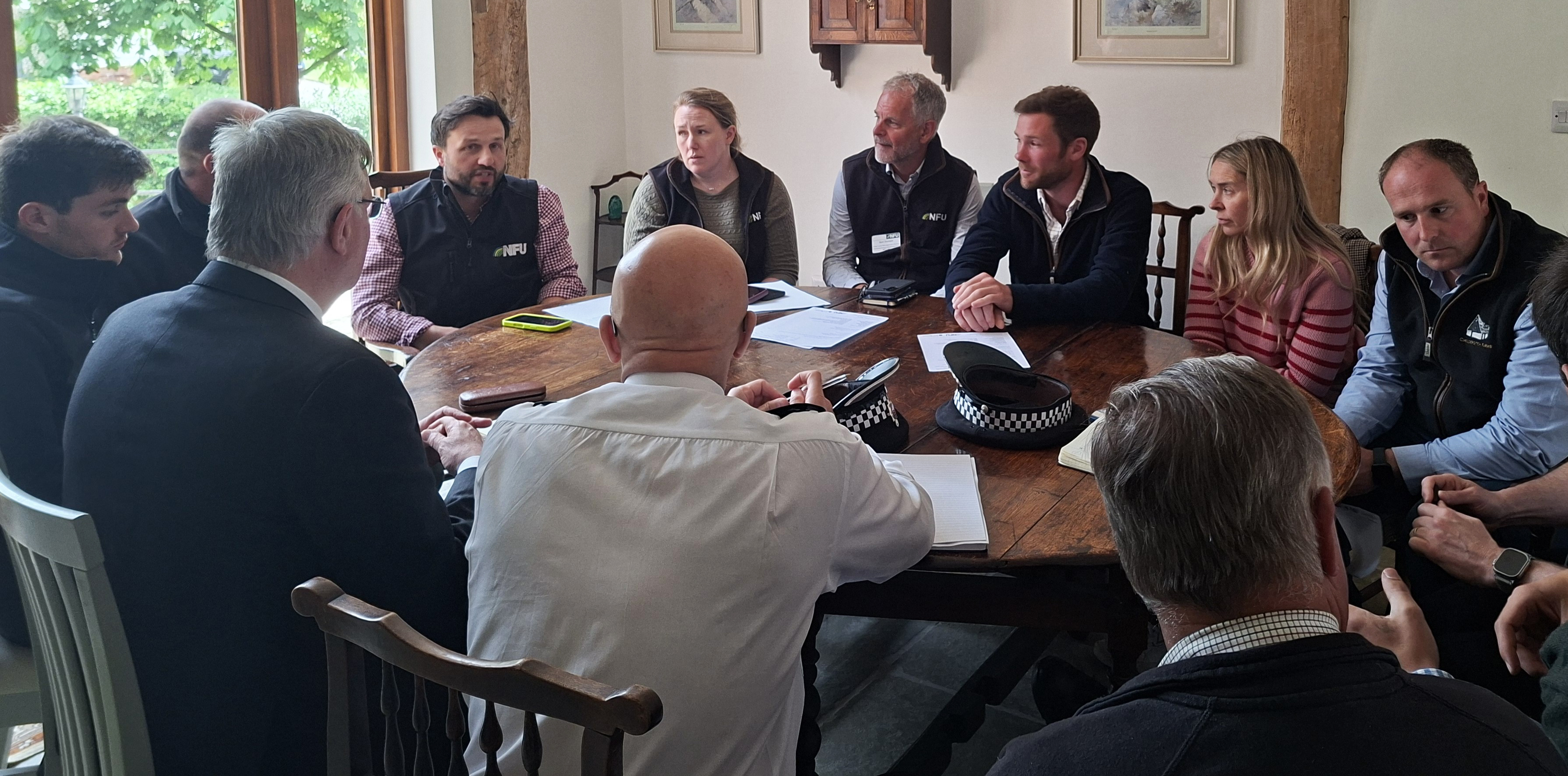 Police and farmers at a round table meeting inside a farmhouse