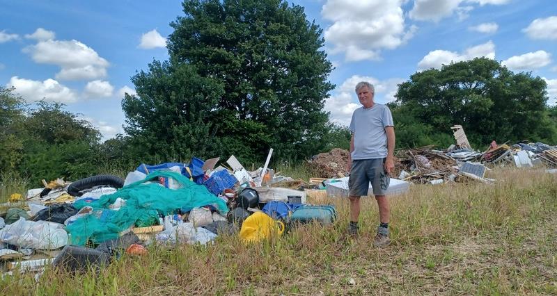 Will Dickinson standing beside fly-tipping on his neighbour's farm