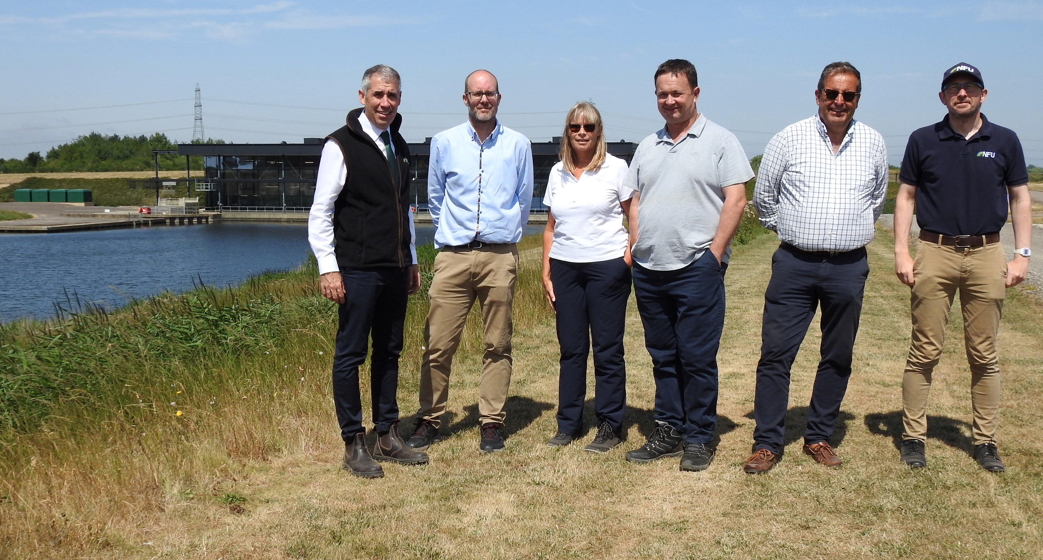Six people standing on a river bank with the St Germans Pumping Station in the background