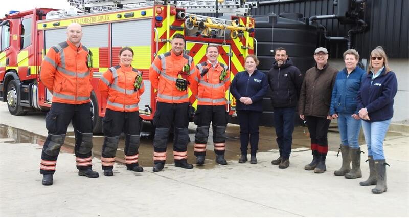 A group of firefighters and farmers in front of a fire engine in a farmyard