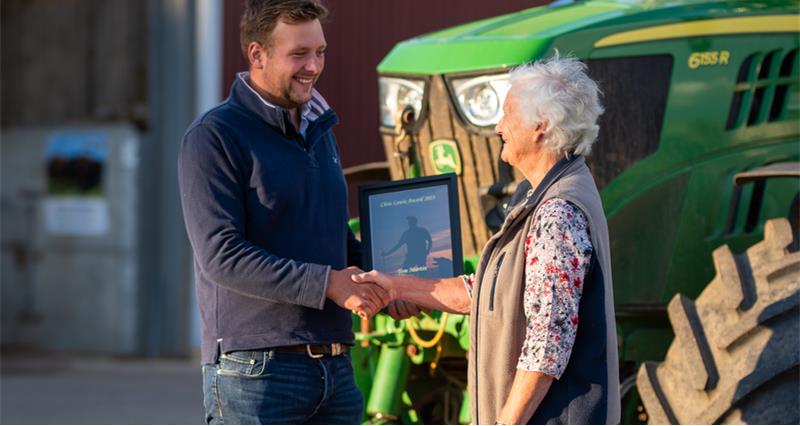 Tom Martin shaking hands with Jane Lewis in front of a tractor.