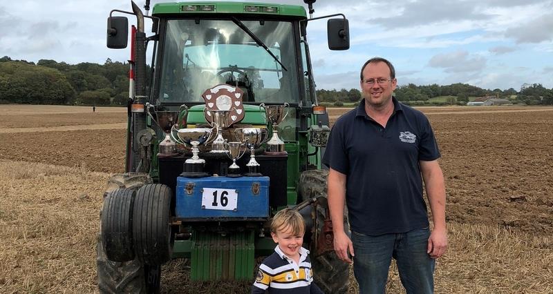 Will Tupper and young son Arthur standing in front of a tractor in a field with ploughing trophies on the tractor bonnet