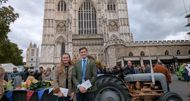 Jessica Stewart and Joe Bramall stood outside Westminster Abbey with a tractor full of British produce behind them