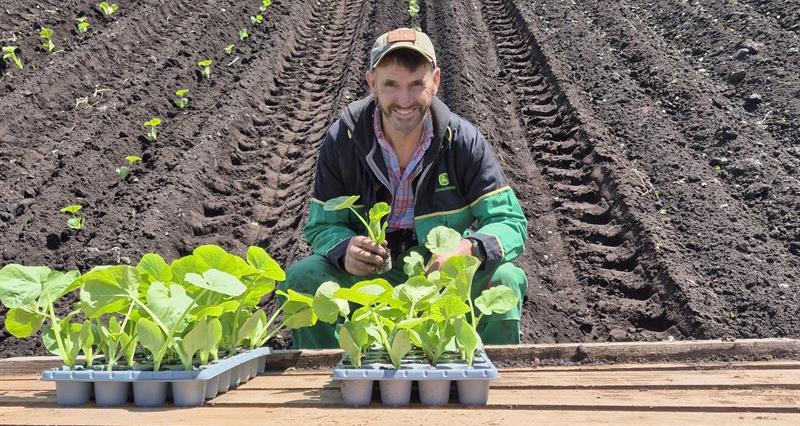 A photo of Kevin Wareing sat at a wooden table on a muddy field during planting