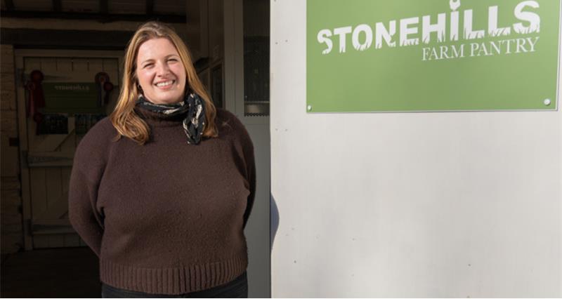 A photo of Anna Riby standing next to a Stonehills Farm Pantry sign