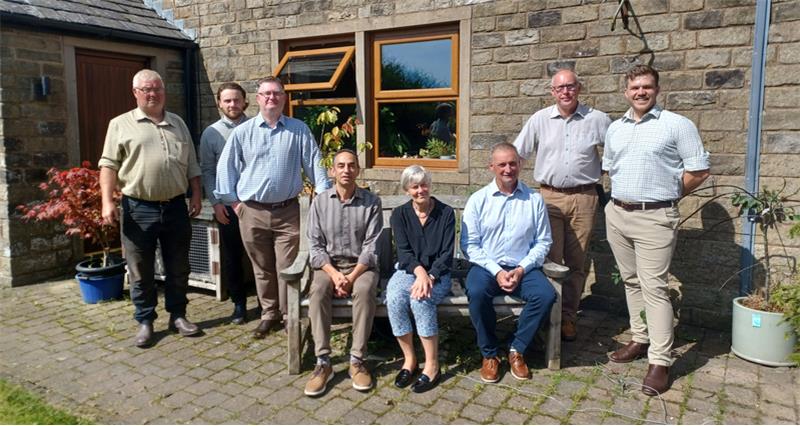 A group photo of NFU North stood and sat on a bench in front of a farm house with Greater Manchester Deputy Mayor Kate Green 