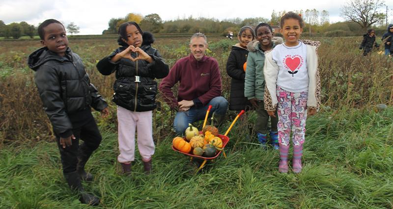 Children pose with a wheelbarrow full of pumpkins