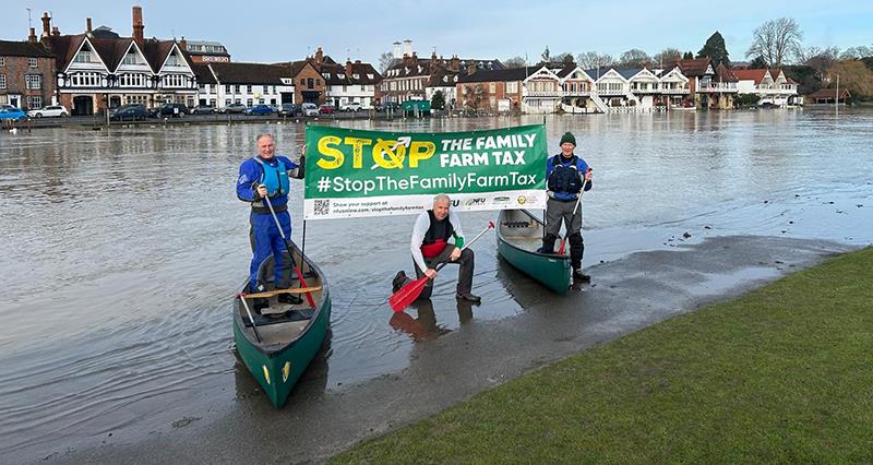 Three farmers beside the River Thames in canoes holding up a Stop the Family Farm Tax banner